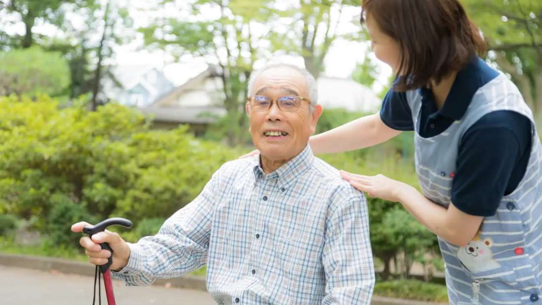 杖をついて歩く男性の肩に手を添えるスタッフ