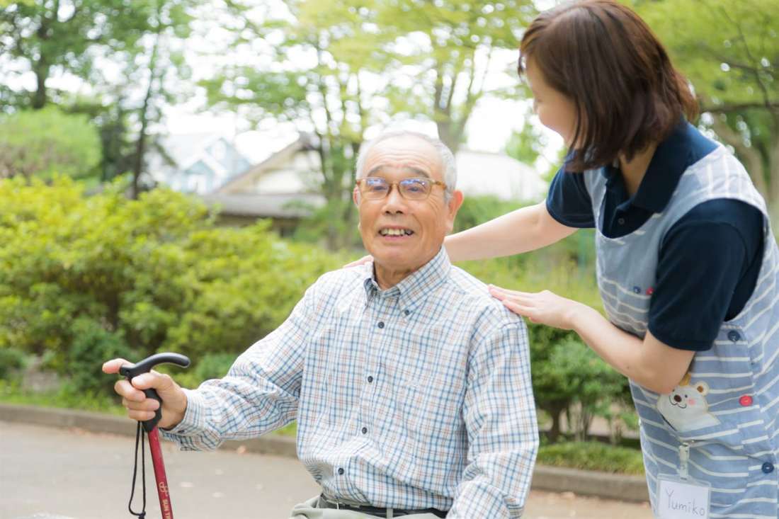 杖をついた男性と並んで公園を歩くスタッフ