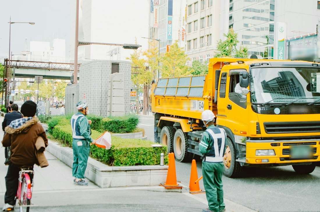 ダンプカーの前で交通誘導をする作業員
