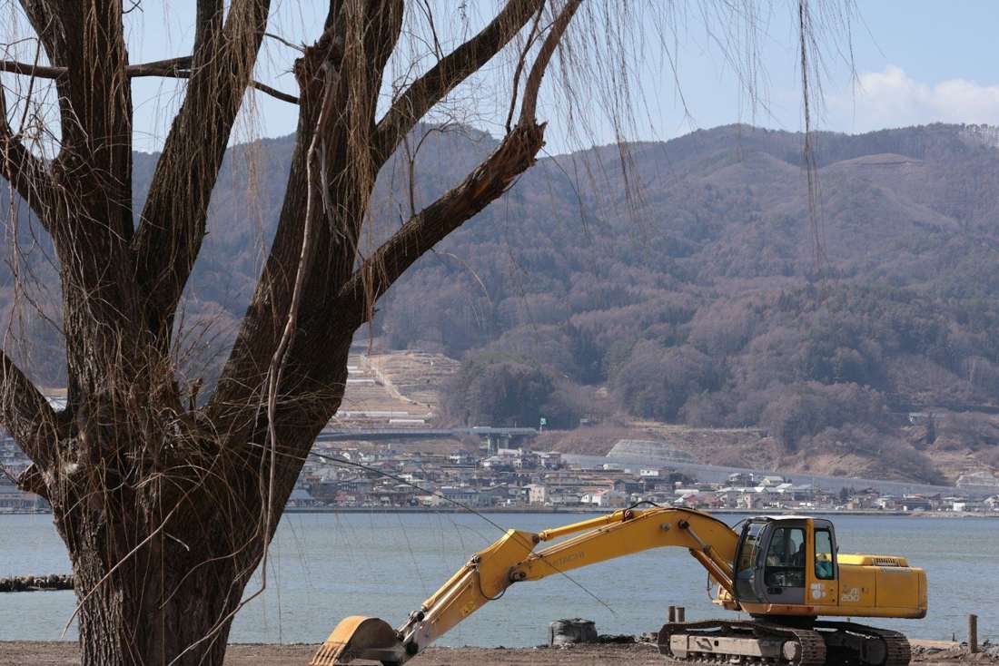 山と湖を背景に作業する油圧ショベル