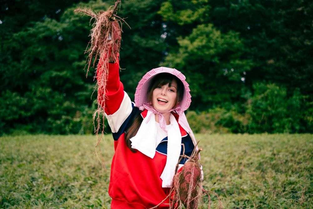 畑で、掘り出したさつまいものつるを笑顔で持ち上げる女性